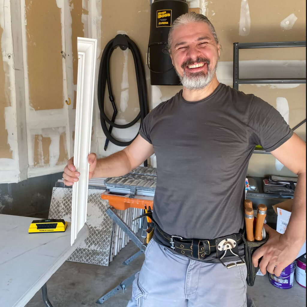 A finish carpenter is holding a piece of trim and smiling to the camera